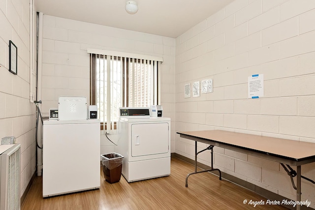 common laundry area with washer and dryer, concrete block wall, and light wood-style floors