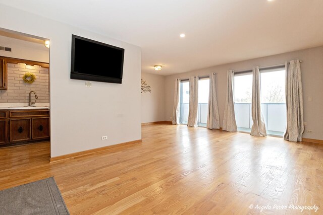 unfurnished living room featuring visible vents, light wood-type flooring, a sink, baseboards, and recessed lighting