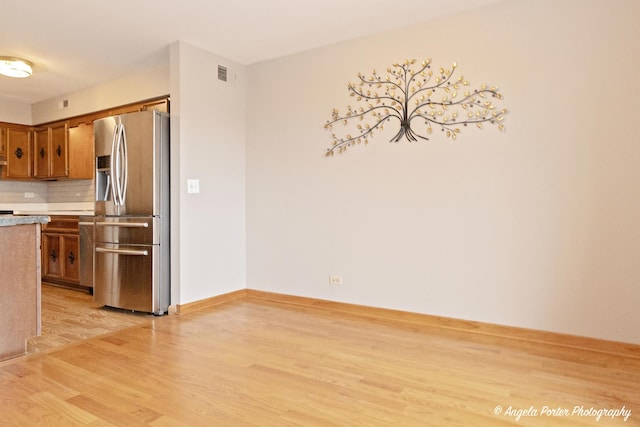 kitchen featuring visible vents, stainless steel refrigerator with ice dispenser, light countertops, light wood-type flooring, and brown cabinets