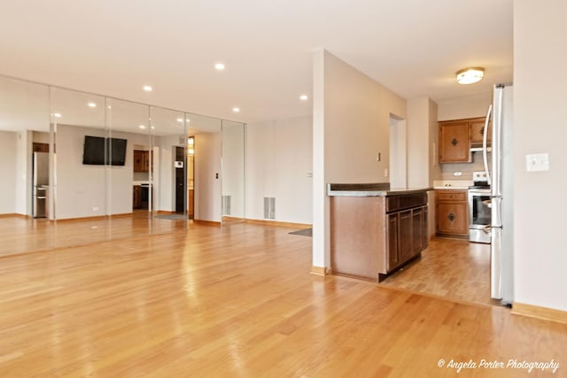 kitchen with brown cabinets, stainless steel appliances, open floor plan, and light wood finished floors
