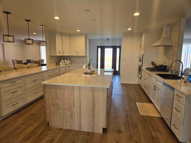 kitchen with appliances with stainless steel finishes, a sink, light stone countertops, and wall chimney exhaust hood