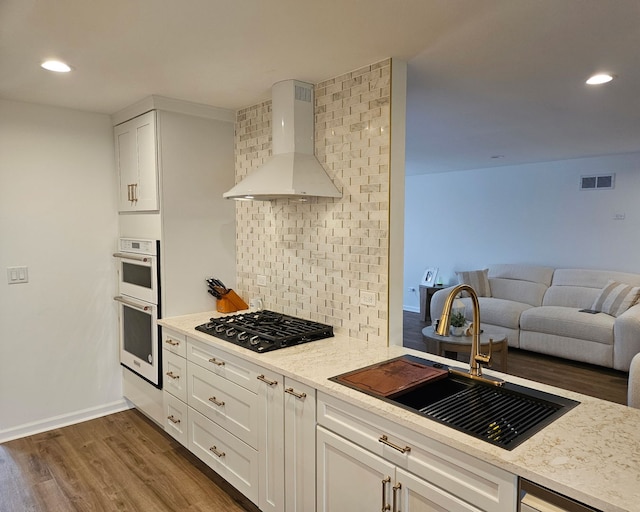 kitchen with decorative backsplash, a sink, visible vents, wall chimney exhaust hood, and black gas cooktop