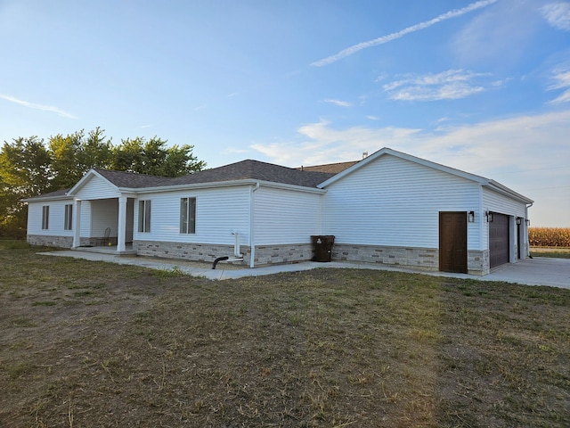 view of side of home with driveway, stone siding, a shingled roof, a yard, and a garage