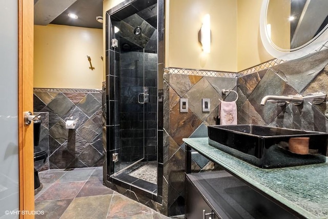 full bath with wainscoting, a shower stall, stone finish floor, and tile walls
