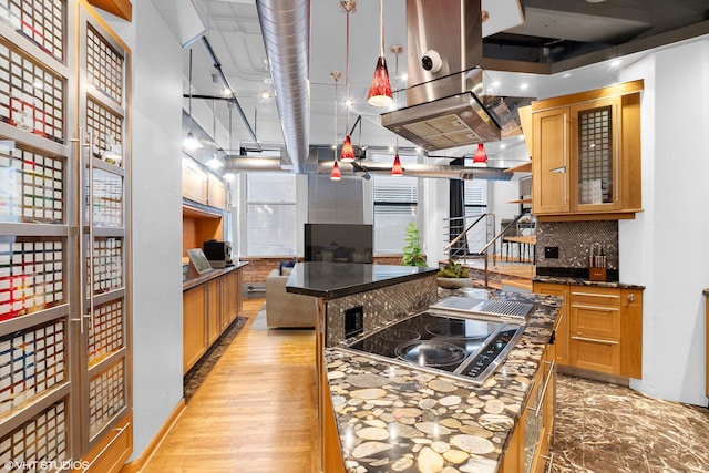 kitchen with decorative backsplash, a kitchen island, pendant lighting, black electric cooktop, and glass insert cabinets