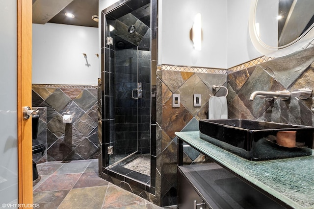 bathroom with wainscoting, vanity, stone finish flooring, tile walls, and a stall shower
