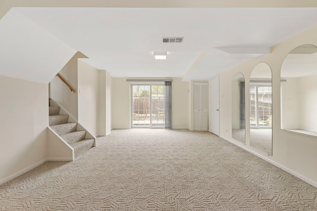 carpeted empty room with arched walkways, baseboards, visible vents, and stairway