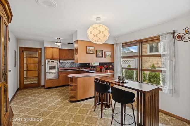 kitchen featuring brown cabinetry, backsplash, a sink, a peninsula, and a warming drawer