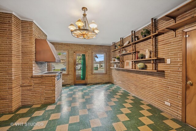 interior space with tile patterned floors, a chandelier, and brick wall