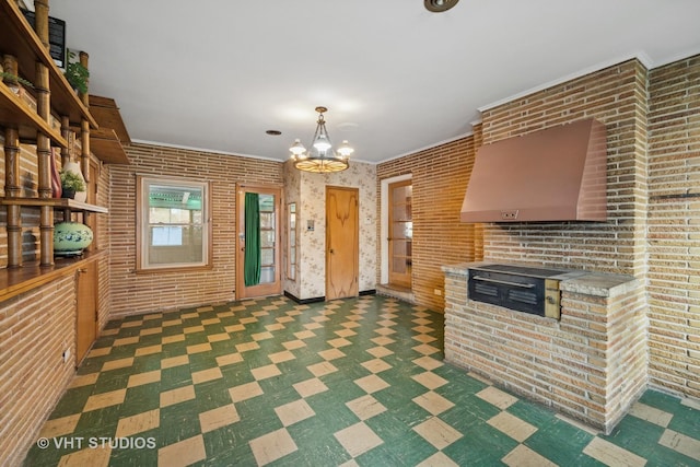 kitchen featuring hanging light fixtures, light countertops, brick wall, a chandelier, and dark floors