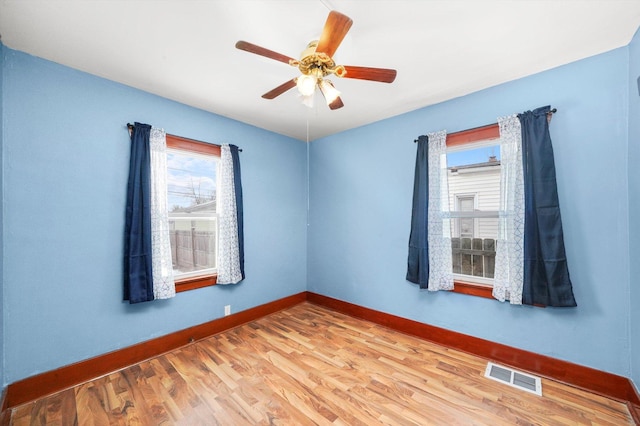 empty room with wood finished floors, visible vents, plenty of natural light, and baseboards