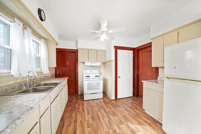 kitchen featuring cream cabinetry, a sink, under cabinet range hood, and white appliances