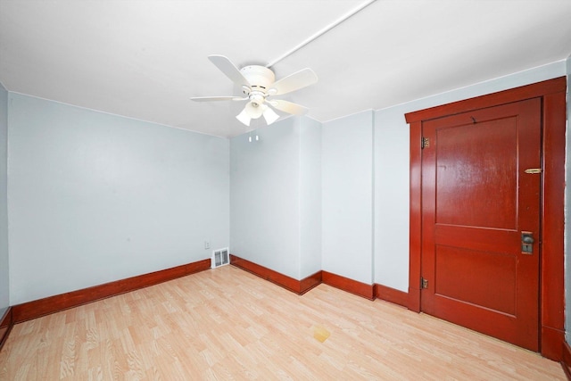 spare room with light wood-type flooring, a ceiling fan, visible vents, and baseboards
