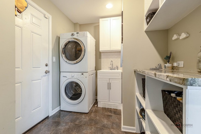 laundry room featuring stacked washer and clothes dryer, a sink, baseboards, and dark tile patterned floors