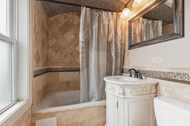 full bath featuring plenty of natural light, tile walls, vanity, toilet, and tiled shower / bath combo