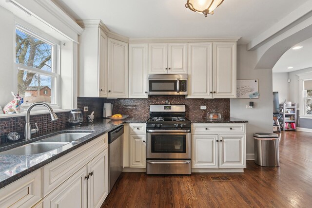 kitchen featuring a sink, arched walkways, a healthy amount of sunlight, and stainless steel appliances