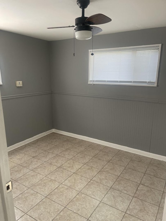 spare room featuring baseboards, ceiling fan, and a wainscoted wall