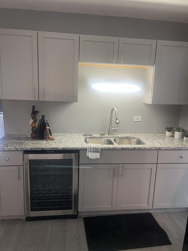 interior space with beverage cooler, light stone counters, a sink, and light wood-style floors
