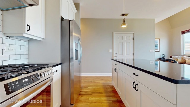 kitchen with stainless steel appliances, dark countertops, decorative backsplash, hanging light fixtures, and light wood-style flooring