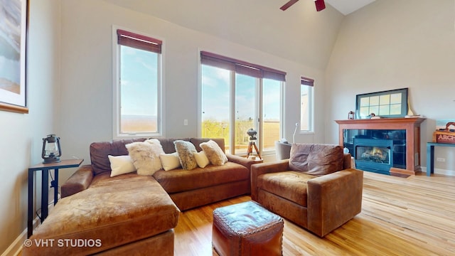 living room featuring light wood finished floors, a fireplace, a ceiling fan, and high vaulted ceiling