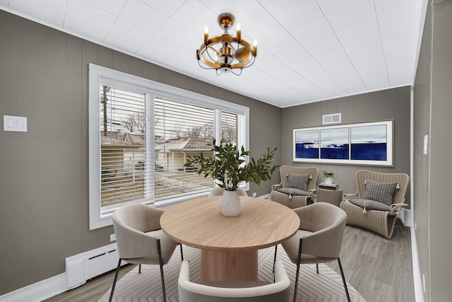 dining room with visible vents, wood walls, baseboards, a chandelier, and light wood finished floors