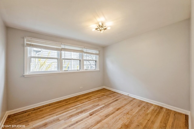 spare room with baseboards, an inviting chandelier, and light wood finished floors