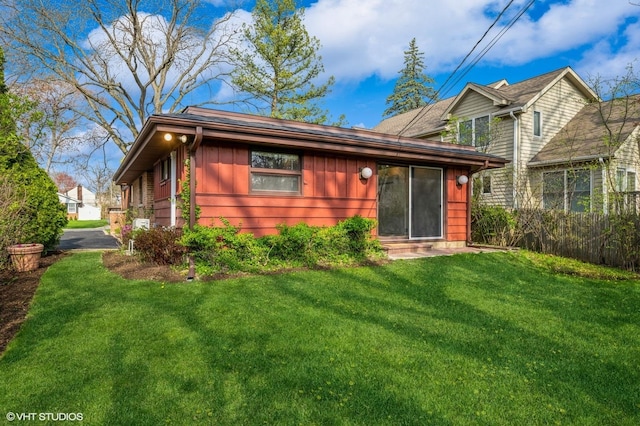 back of house with a lawn, fence, and board and batten siding
