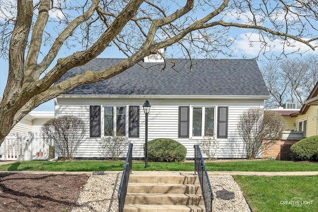 view of front facade with a shingled roof and a front lawn