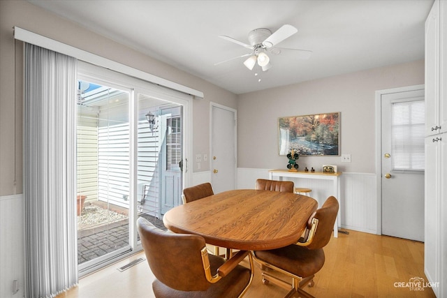 dining room with ceiling fan, visible vents, light wood finished floors, and a wainscoted wall