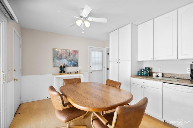 dining area with a ceiling fan, light wood finished floors, and a wainscoted wall
