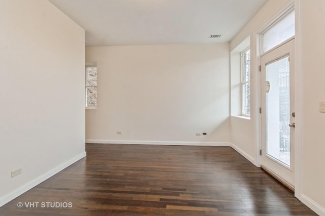 empty room featuring baseboards, dark wood-style flooring, and visible vents