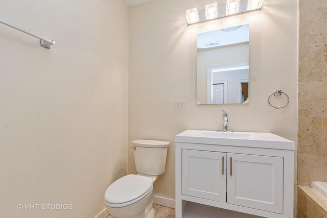 bathroom with visible vents, vanity, toilet, baseboards, and tiled tub