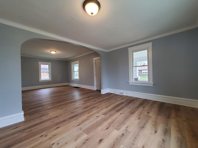 spare room with crown molding, arched walkways, baseboards, and wood finished floors