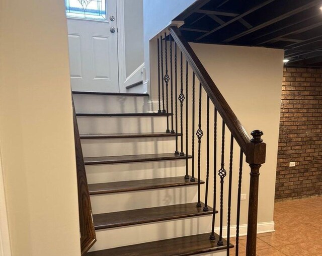 stairway with brick wall and tile patterned floors