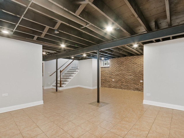 below grade area with baseboards, brick wall, and stairway