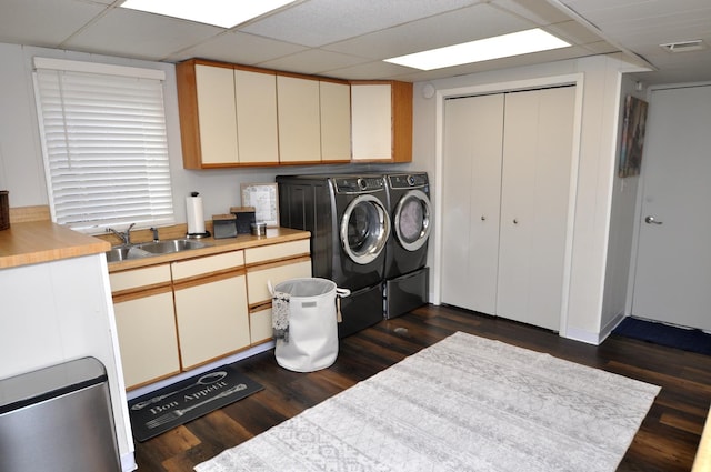 laundry area featuring washing machine and clothes dryer, cabinet space, a sink, dark wood-type flooring, and visible vents