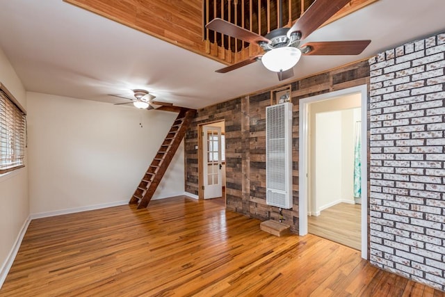 empty room with baseboards, a ceiling fan, a heating unit, and wood finished floors