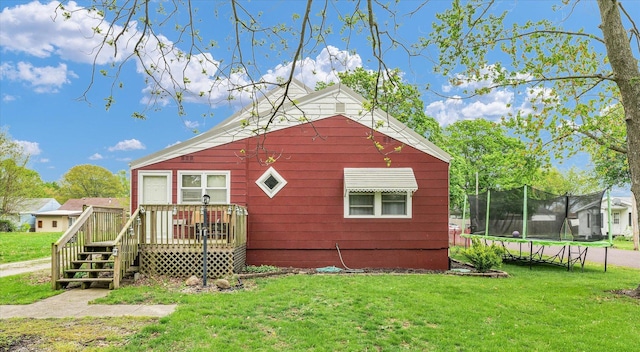 back of house with a deck, a trampoline, and a lawn