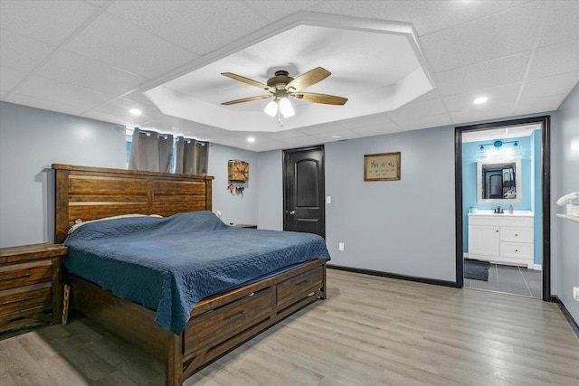 bedroom with baseboards, ensuite bath, light wood-style flooring, and a ceiling fan