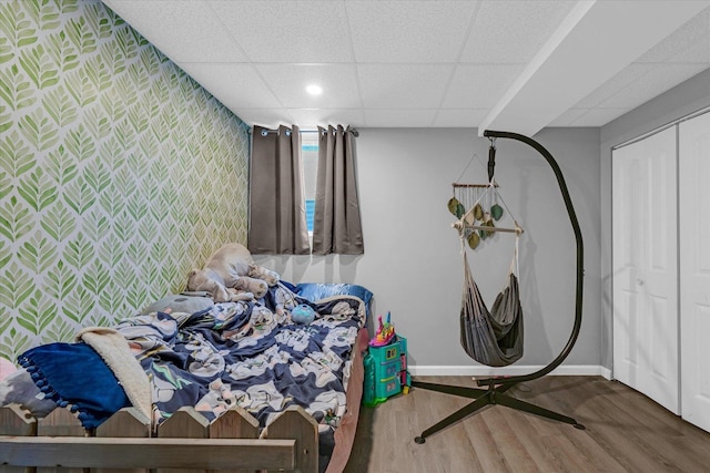bedroom with wallpapered walls, baseboards, an accent wall, wood finished floors, and a paneled ceiling