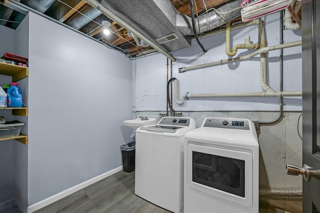 clothes washing area featuring wood finished floors, a sink, laundry area, visible vents, and independent washer and dryer