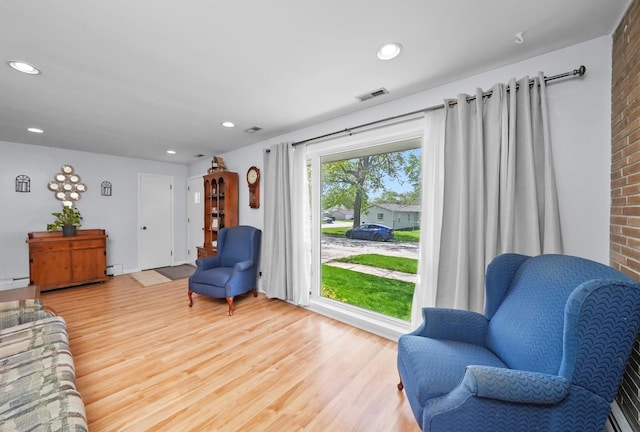 sitting room with light wood-type flooring, a baseboard heating unit, recessed lighting, and brick wall