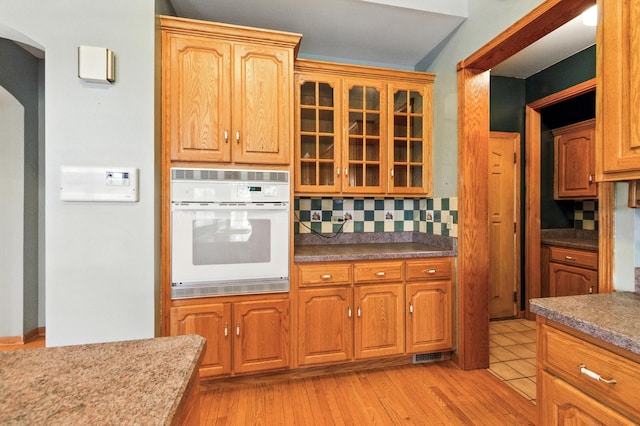 3664 E 2619th Rd, Sheridan, IL 60551 - kitchen with white oven, tasteful backsplash, glass insert cabinets, arched walkways, and light wood-type flooring