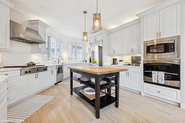 117 Iroquois Dr, Clarendon Hills, IL 60514 - kitchen featuring stainless steel appliances, wall chimney range hood, light wood finished floors, a sink, and decorative light fixtures
