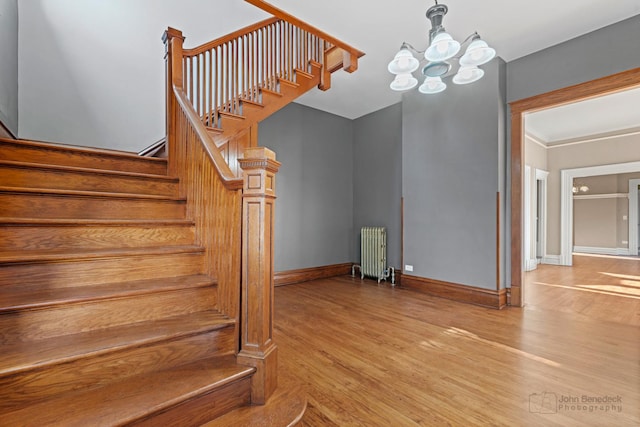 stairway with radiator heating unit, wood finished floors, a chandelier, and baseboards