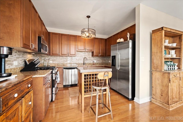 kitchen featuring stainless steel appliances, decorative backsplash, light wood-style flooring, and a kitchen bar