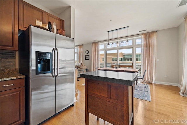 kitchen featuring light wood-style floors, baseboards, a kitchen island, stainless steel refrigerator with ice dispenser, and visible vents