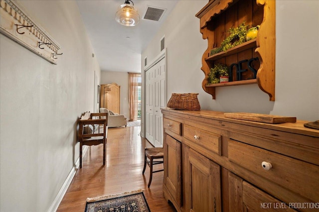 hall featuring visible vents, baseboards, and wood finished floors