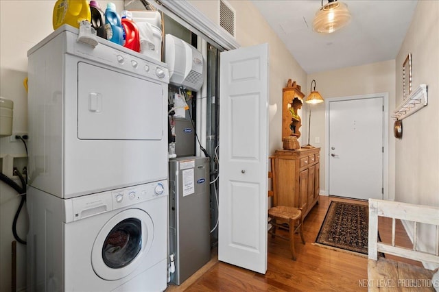 clothes washing area with visible vents, stacked washer and clothes dryer, wood finished floors, and laundry area