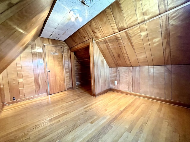 bonus room with wooden walls, vaulted ceiling, and wood finished floors